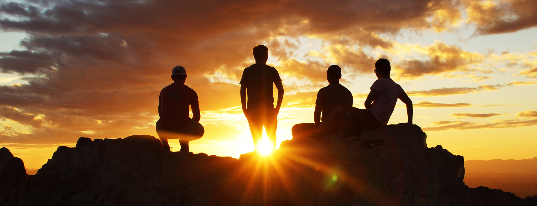 Four people watching the sunset from the top of a rock